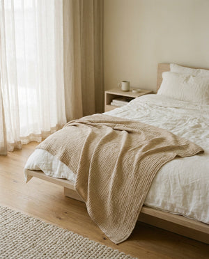 Livnorr muslin throw blanket draped over bed in Scandinavian bedroom with morning light